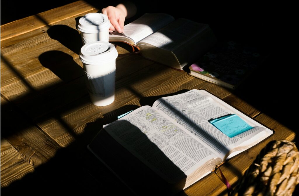 Open bibles and notes on a wooden table with coffee cups.