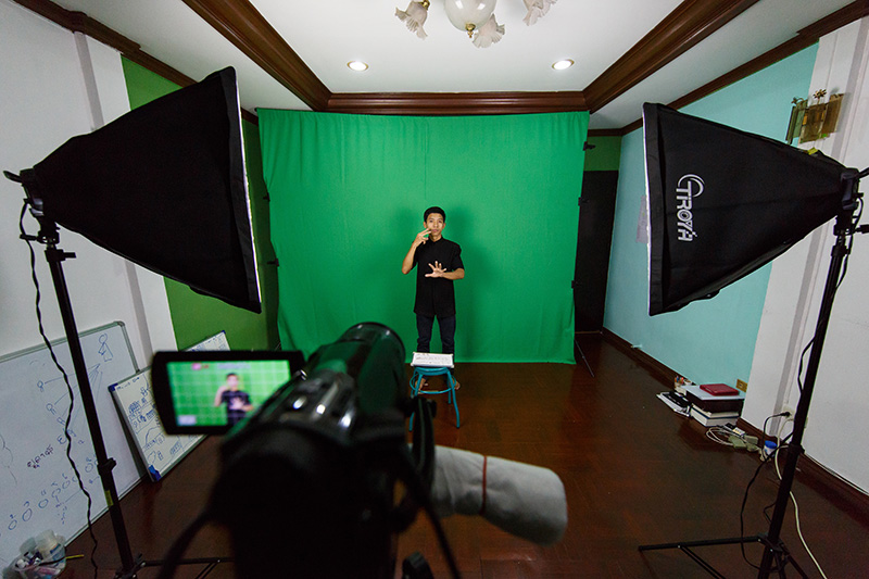 Man signing in front of a green screen for camera.