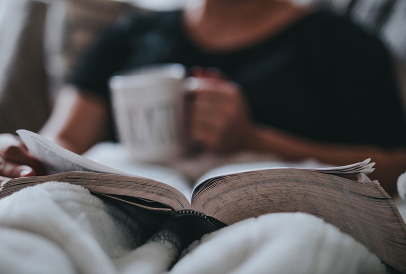 Person in bed with a blanket, Bible and drink cup.