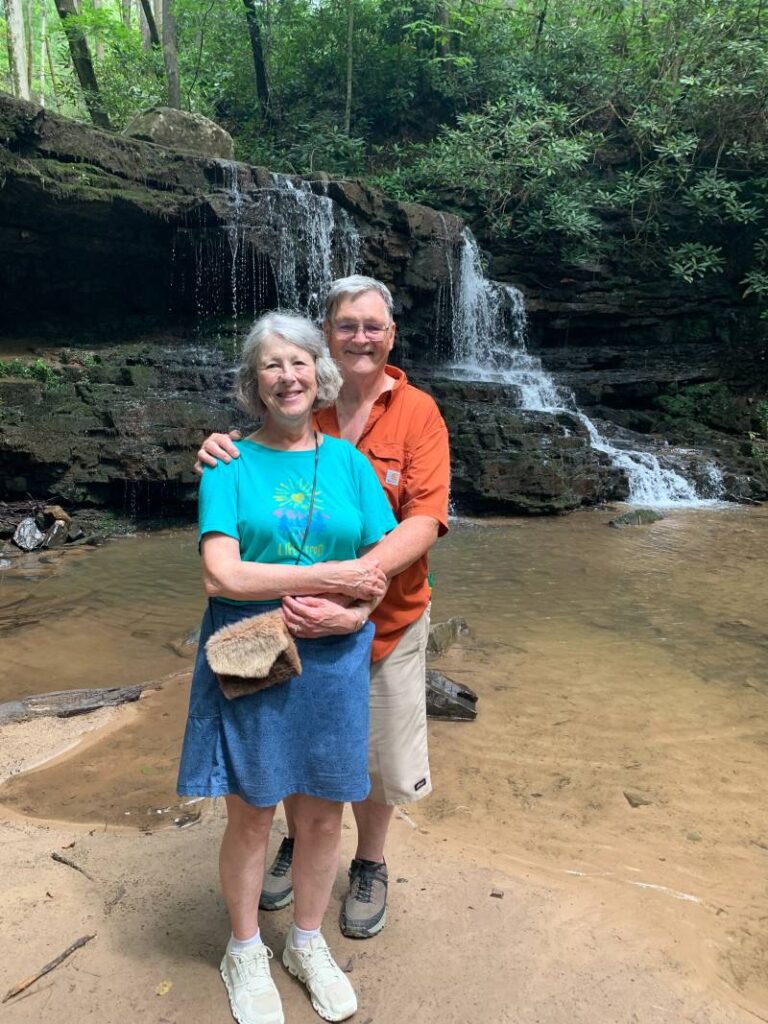 Beverly with her husband in front of a waterfall.