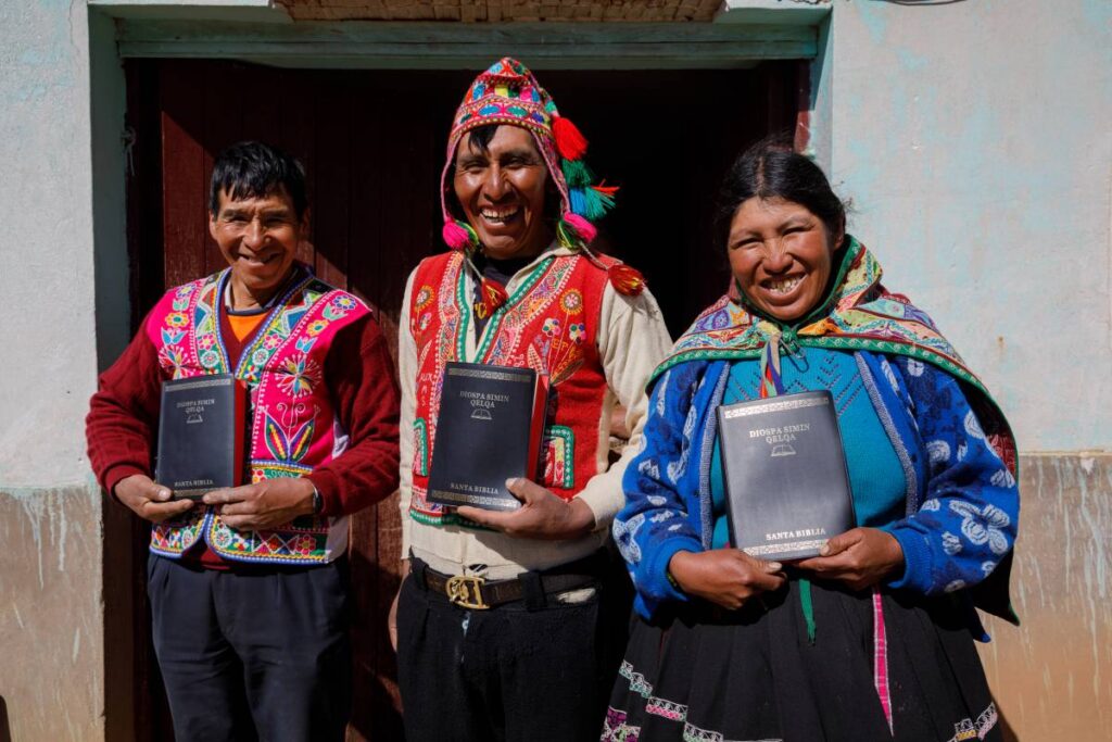 Two men and a woman smile as they pose with the Quechua Bible they have just received during a literacy class in Ch'aqoyo, Peru.