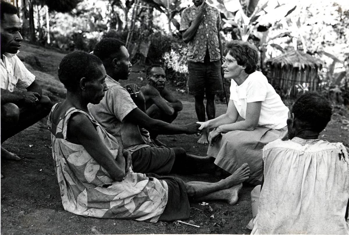 Historical photo from Papua New Guinea of a woman talking to a group of community members.