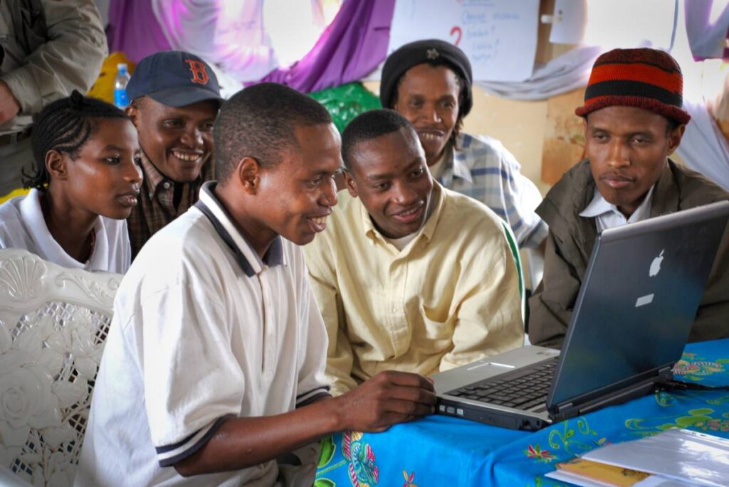 A group of people gather at a computer during a writer workshop in Kondoa.